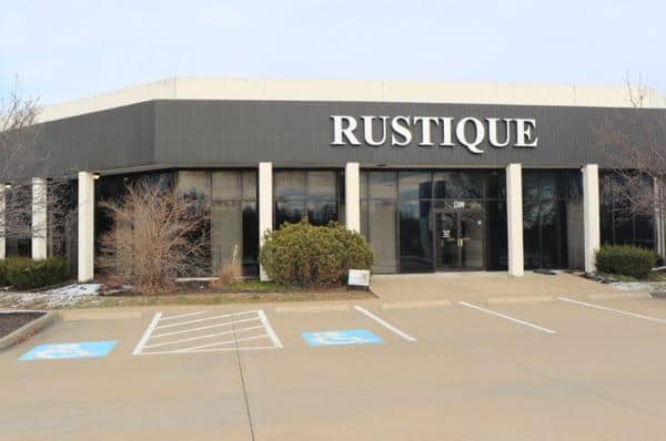 A modern building with the sign "RUSTIQUE" has large windows, surrounded by landscaping, featuring a parking area with accessible spaces in front.